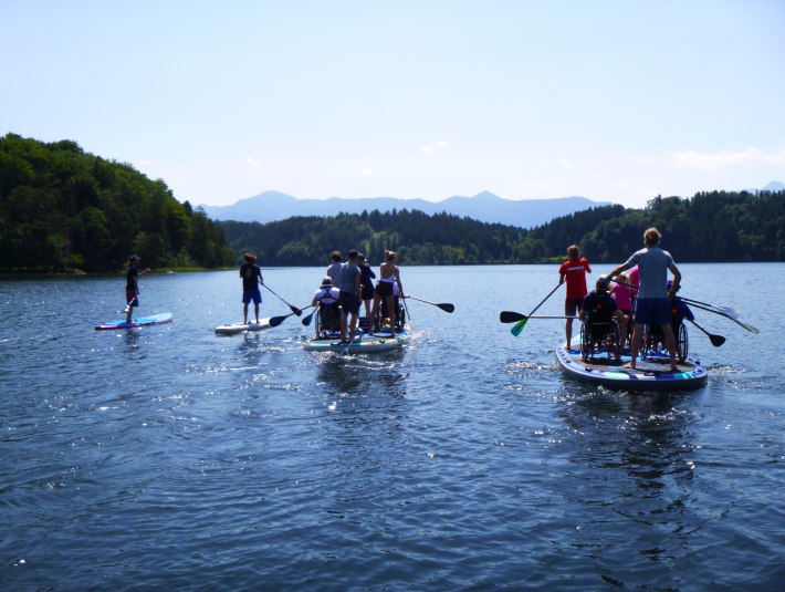 Menschen mit Rollstuhl auf einem SUP auf dem See, © SUP Verleih Staffelsee Menschen mit Rollstuhl auf einem SUP auf dem See, © SUP Verleih Staffelsee